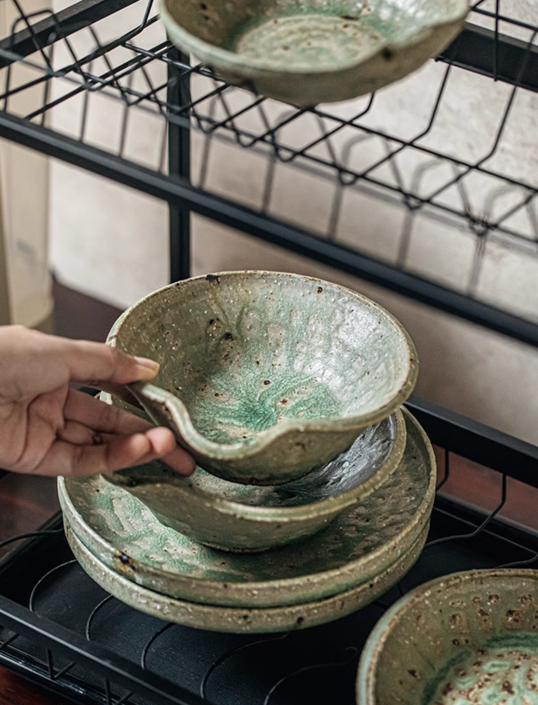 Artisan Green Dinnerware bowls and plates stacked on a drying rack, textured ceramic home decor.